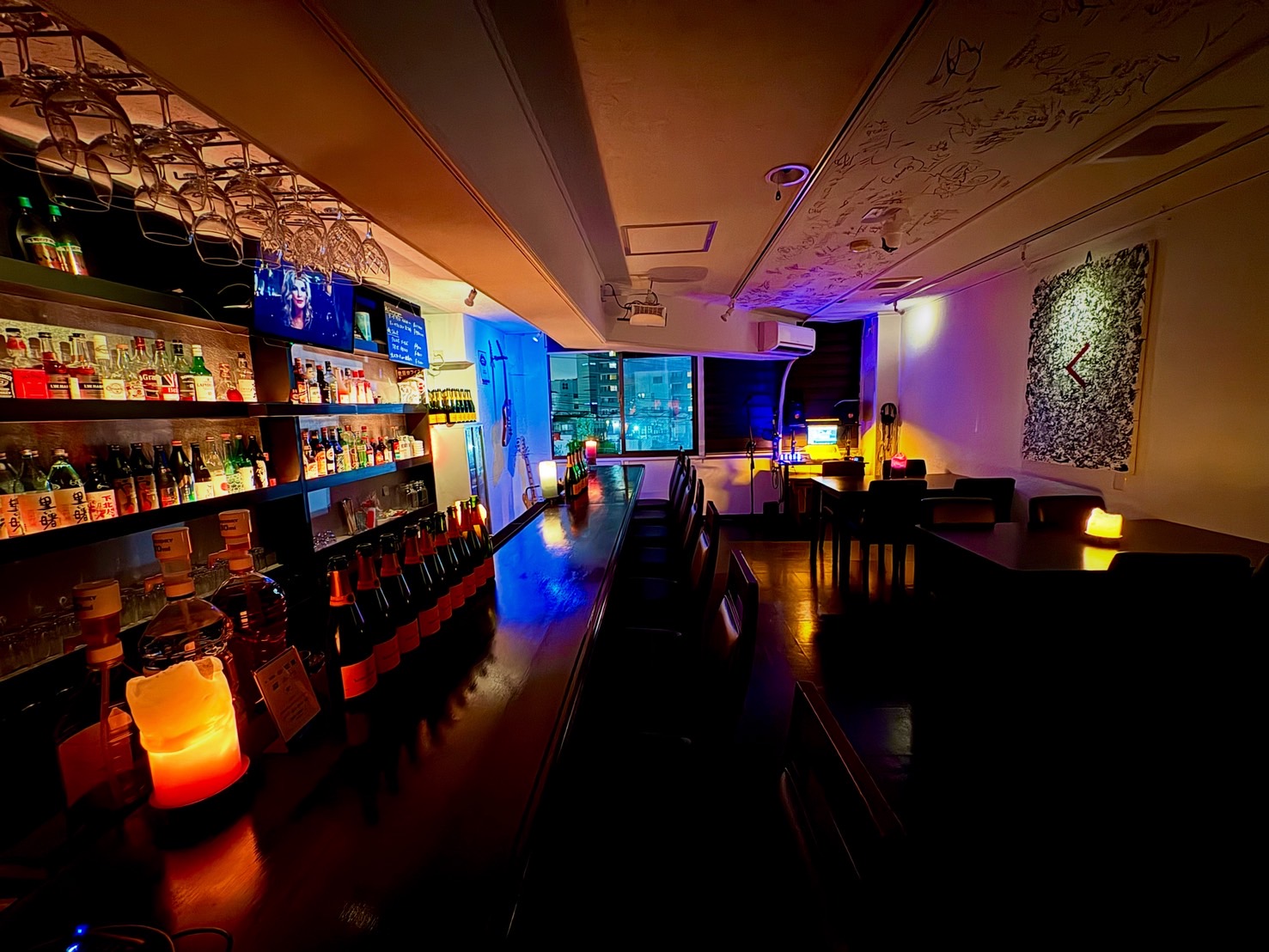 BAR ENSEMBLEの店内。キャンドルの灯るカウンターと酒棚、奥にテーブル席。天井には来店した人たちのサインが描かれている