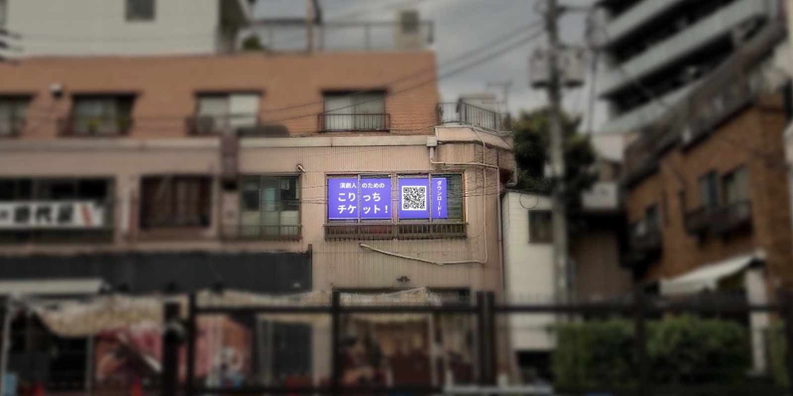 通りから見た建物。2階の窓に「演劇人のための こりっちチケット！」とQRコードを表示した窓面LEDビジョンがあり、枠で囲んで示している